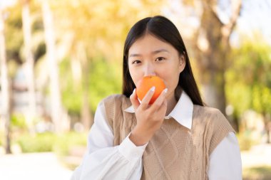 Açık havada elinde portakal tutan güzel bir Çinli kadın.