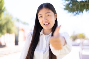 Dışarıda güzel bir Çinli kadın var. Başparmakları havada. Çünkü iyi bir şey oldu.