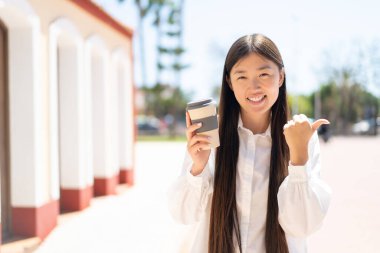 Güzel bir Çinli kadın açık havada kahve alıp bir ürün sunmak için kenarı işaret ediyor.