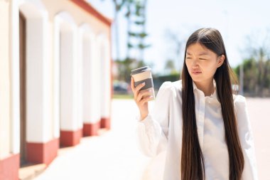 Güzel bir Çinli kadın üzgün bir ifadeyle açık havada kahve tutuyor.