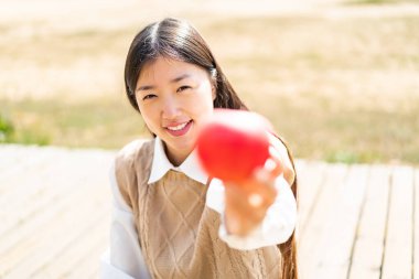 Açık havada genç bir Çinli kadın elinde mutlu bir ifadeyle bir elma tutuyor.