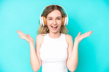 Sarışın İngiliz genç kız mavi arka planda izole edilmiş şaşırmış ve müzik dinliyor.