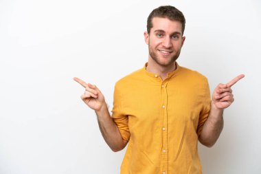 Beyaz arka planda izole edilmiş genç beyaz adam parmak uçlarını işaret ediyor ve mutlu.