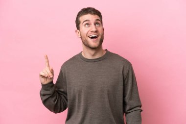 Pembe arka planda izole edilmiş genç beyaz adam yukarı bakıyor ve şaşırıyor.