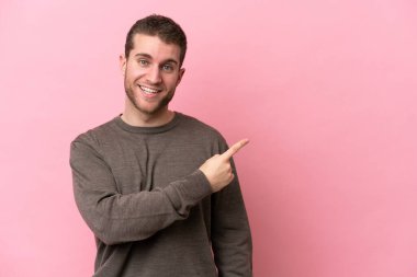 Pembe arka planda izole edilmiş genç beyaz adam şaşırmış ve işaret ediyor.