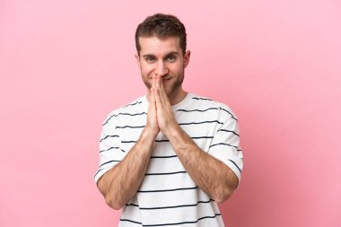 Pembe arka planda izole edilmiş genç beyaz adam avuç içlerini bir arada tutuyor. İnsan bir şey ister.