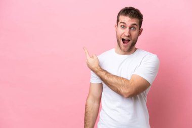 Pembe arka planda izole edilmiş genç beyaz adam şaşırmış ve işaret ediyor.