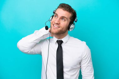 Tele pazarlamacı beyaz bir adam mavi arka planda izole edilmiş bir kulaklıkla çalışıyor.