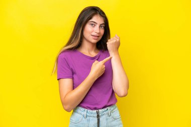 Sarı arka planda izole genç beyaz kadın geç kalma jesti yapıyor.