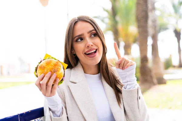 Młoda Ładna Kobieta Trzymając Hamburgera Świeżym Powietrzu Zamiarem Realizacji Rozwiązania — Zdjęcie stockowe
