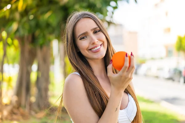 stock image Young woman at outdoors holding an orange with happy expression