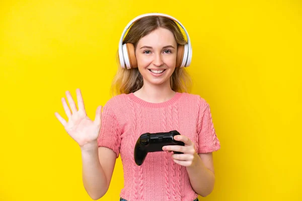 ブロンド英国の若い女の子は 指で5を数える黄色の背景に隔離されたビデオゲームコントローラーで遊んでいます — ストック写真