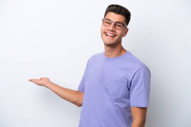 Beyaz arka planda soyutlanmış beyaz tenli genç adam davet edilmek için ellerini yana uzatıyor.