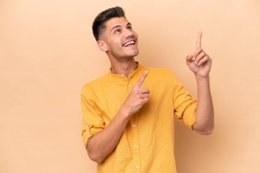 Young caucasian man isolated on beige background pointing with the index finger a great idea