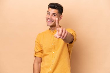 Beyazlı genç bir adam bej arka planda izole edilmiş ve parmağını kaldırıyor.