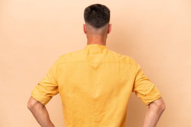 Young caucasian man isolated on beige background in back position