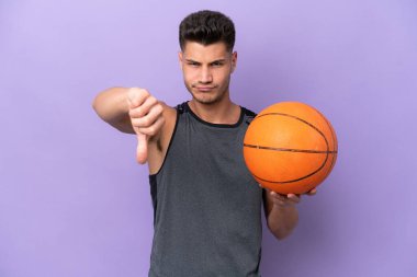 Genç beyaz kadın basketbolcu, mor arka planda izole edilmiş, negatif ifadeli baş parmağını gösteriyor.