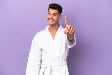Mor arka planda karate yapan genç beyaz adam parmağını kaldırıyor ve gösteriyor.