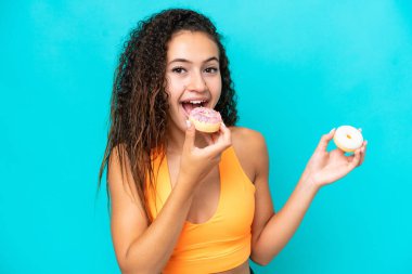 Genç bir Arap kadın mavi arka planda izole edilmiş donut yiyor.