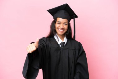Kolombiyalı genç bir üniversite mezunu pembe arka planda izole edilmiş bir şekilde el kol hareketi yapıyor.