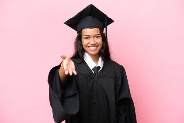 Üniversiteden mezun genç bir Kolombiyalı kadın pembe arka planda izole edilmiş ve iyi bir anlaşma için el sıkışıyor.