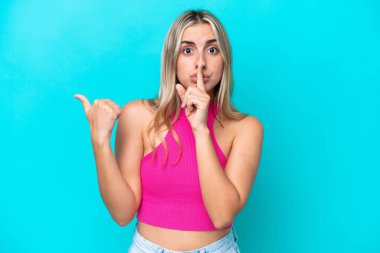 Mavi arka planda izole edilmiş genç, beyaz bir kadın. Yan tarafı işaret ediyor ve sessiz hareketler yapıyor.