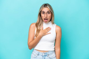 Mavi arka planda izole edilmiş genç beyaz kadın kendini işaret ediyor.