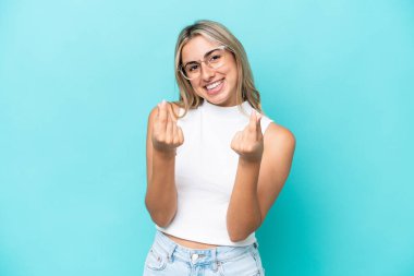 Mavi arka planda izole genç beyaz kadın para hareketi yapıyor.