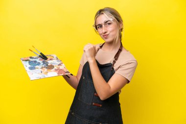 Sarı arka planda kendini beğenmiş ve gururlu bir palet tutan beyaz bir kadın.