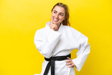 Young caucasian woman doing karate isolated on yellow background thinking an idea while looking up