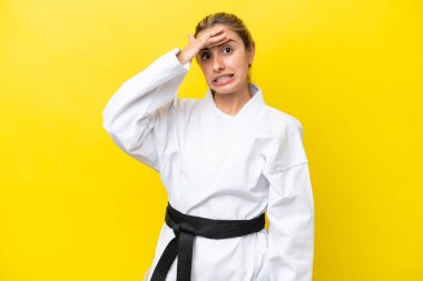 Sarı arka planda karate yapan beyaz bir kadın. Yan tarafa bakarken sürpriz jest yapıyor.