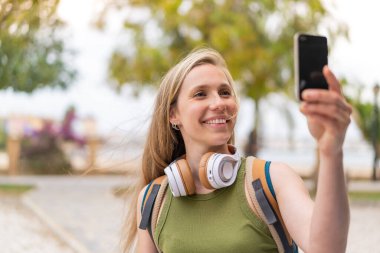 Açık havada selfie çeken genç sarışın kadın.