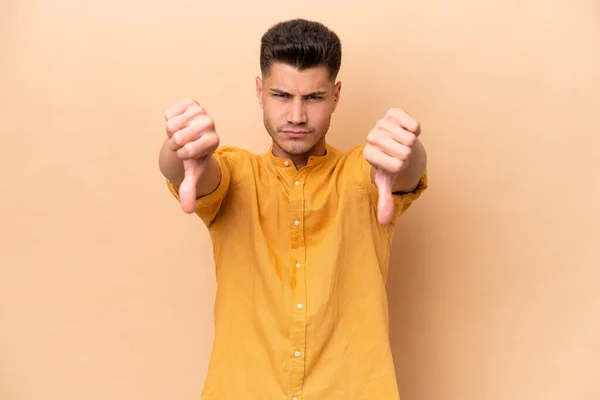 Young Caucasian Man Isolated Beige Background Showing Thumb Two Hands — Stockfoto