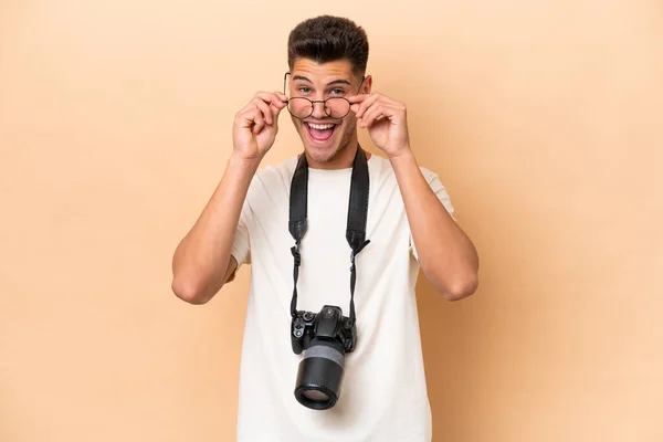 Νεαρός Φωτογράφος Καυκάσιος Άνδρας Απομονωμένος Μπεζ Φόντο Γυαλιά Και Έκπληκτος — Φωτογραφία Αρχείου