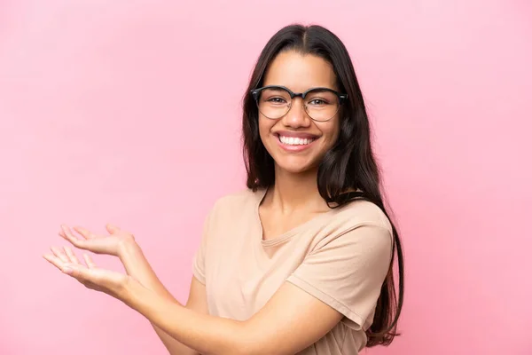 Junge Kolumbianerin Isoliert Auf Rosa Hintergrund Mit Brille Und Präsentiert — Stockfoto