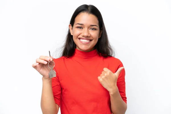 年轻的哥伦比亚女人拿着家里的钥匙 用白色的背景隔开 指向侧面来展示自己的产品 — 图库照片