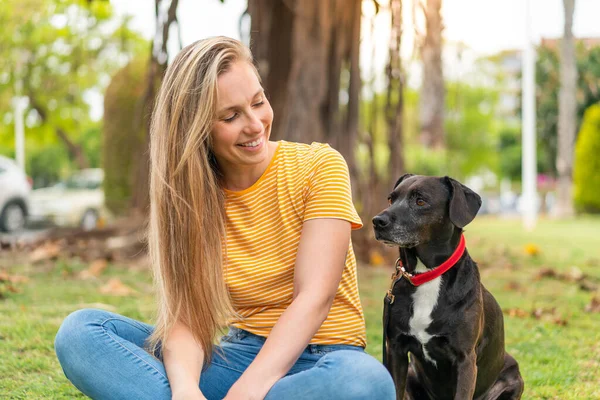 Dışarıda sevimli siyah köpeği olan genç sarışın kadın.