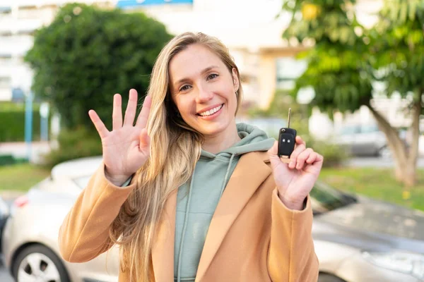 若い金髪の女性は 幸せな表情で手で塩漬けで屋外で車のキーを保持しています — ストック写真