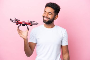 Genç Brezilyalı bir adam pembe arka planda izole edilmiş mutlu bir ifadeyle İHA tutuyor.