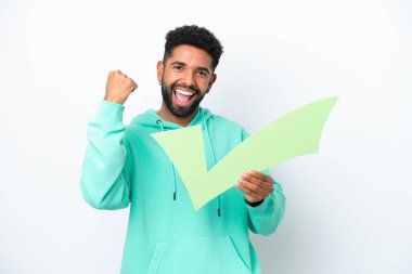 Young Brazilian man isolated on white background holding a check icon and celebrating a victory