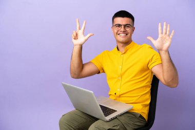 Dizüstü bilgisayarlı bir sandalyede oturan genç adam parmaklarıyla sekiz tane sayıyor.