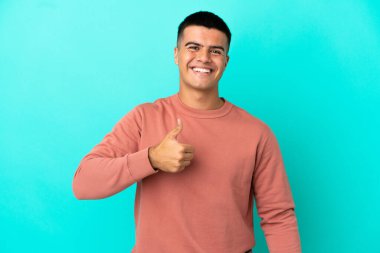 Soyutlanmış mavi arka planda genç yakışıklı bir adam baş parmak işareti yapıyor.