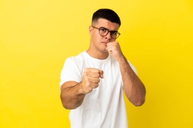 Genç, yakışıklı, izole edilmiş sarı arka planda dövüşen bir adam.