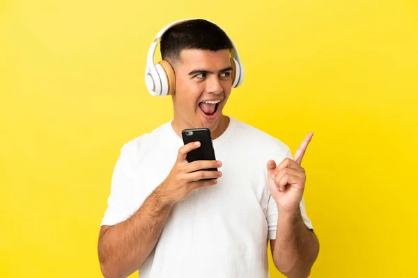 年轻英俊的男子在孤独的黄色背景上 一边用手机一边听着音乐 一边唱歌 — 图库照片