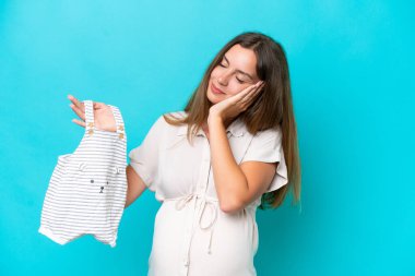 Young caucasian woman isolated on blue background pregnant and holding baby clothes