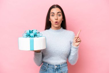 Young caucasian woman holding birthday cake isolated on pink background intending to realizes the solution while lifting a finger up
