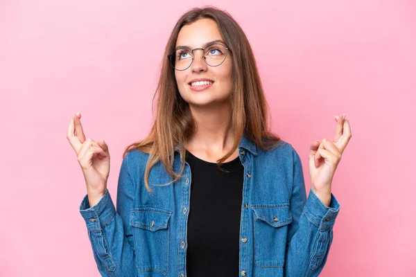 Young caucasian woman isolated on pink background with fingers crossing and wishing the best
