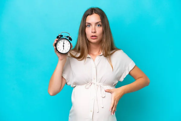 Νεαρή Καυκάσια Γυναίκα Απομονωμένη Μπλε Φόντο Έγκυος Και Κρατώντας Ρολόι — Φωτογραφία Αρχείου