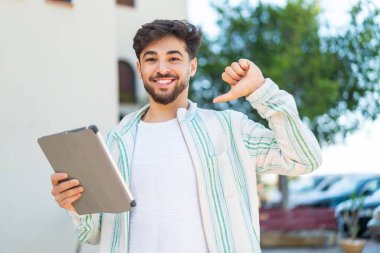 Dışarıda elinde tablet tutan yakışıklı bir Arap gururlu ve kendini beğenmiş.