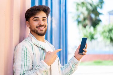 Yakışıklı bir Arap açık havada cep telefonu kullanıyor ve onu işaret ediyor.